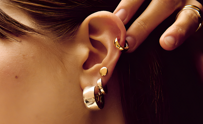Stacked gold hoop and stud earrings on a female model